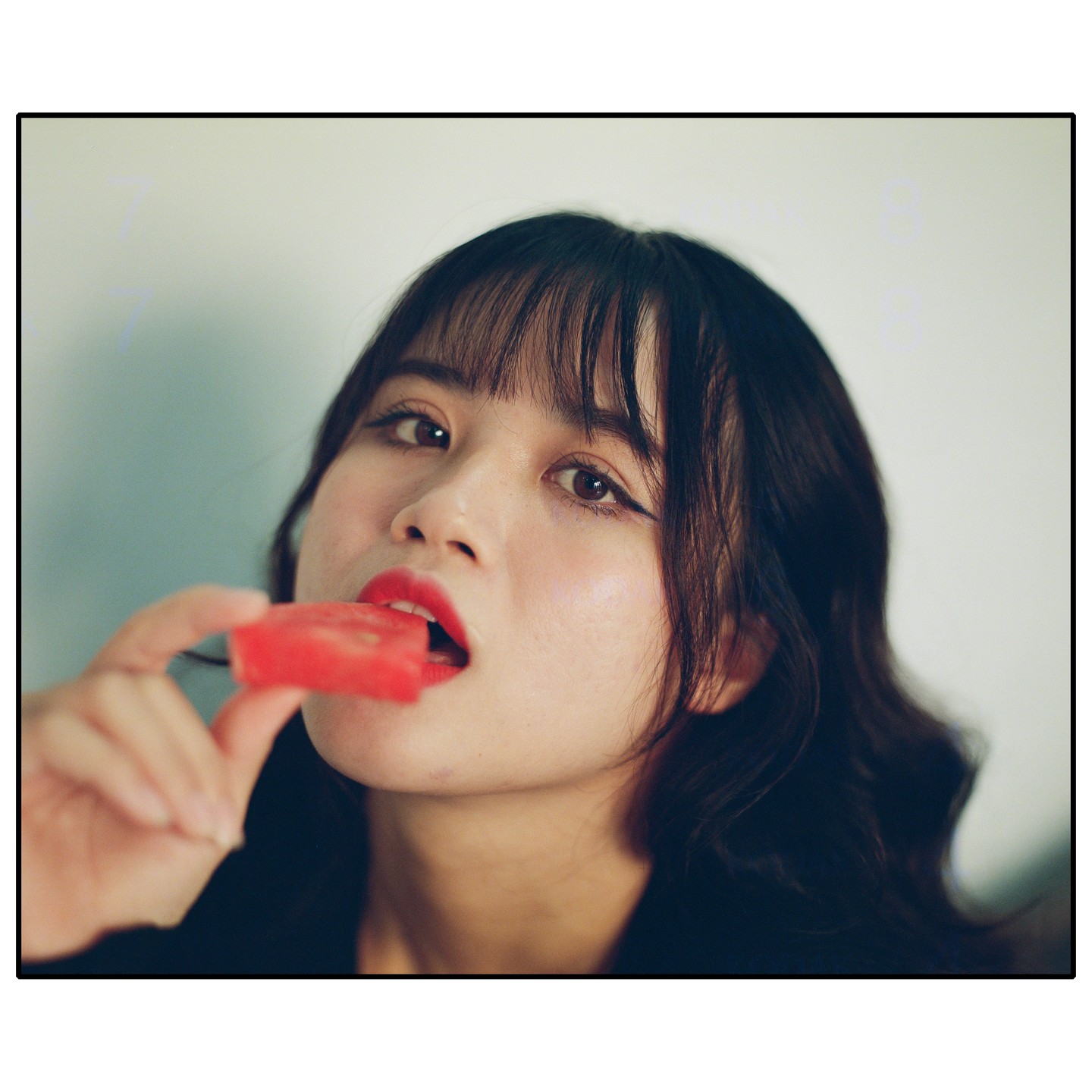 A woman with bangs and red lipstick holds a piece of watermelon to her mouth.