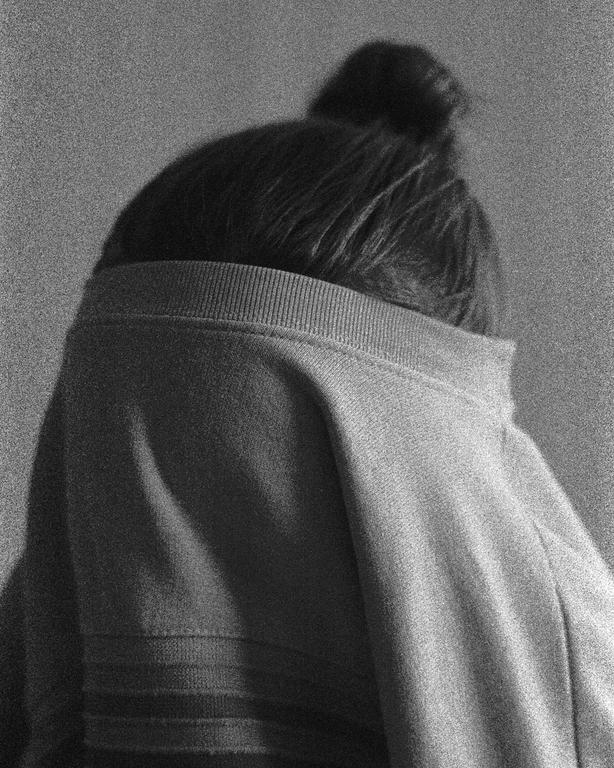 A person with a bun in their hair is seen from behind, wearing a sweater pulled up to cover their head.