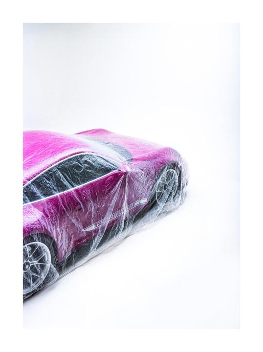 A pink toy car is covered in plastic wrap against a white background.