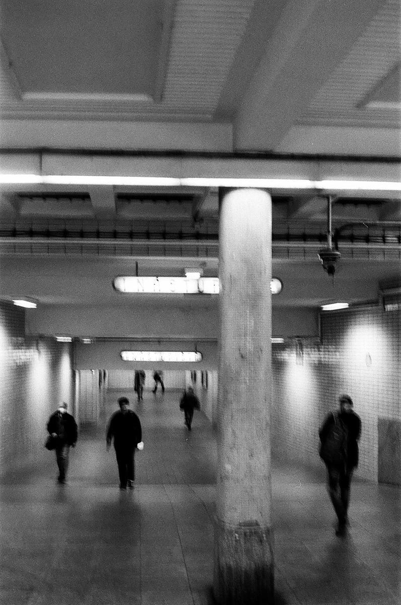 People walk through a subway tunnel with a large pillar in the foreground.