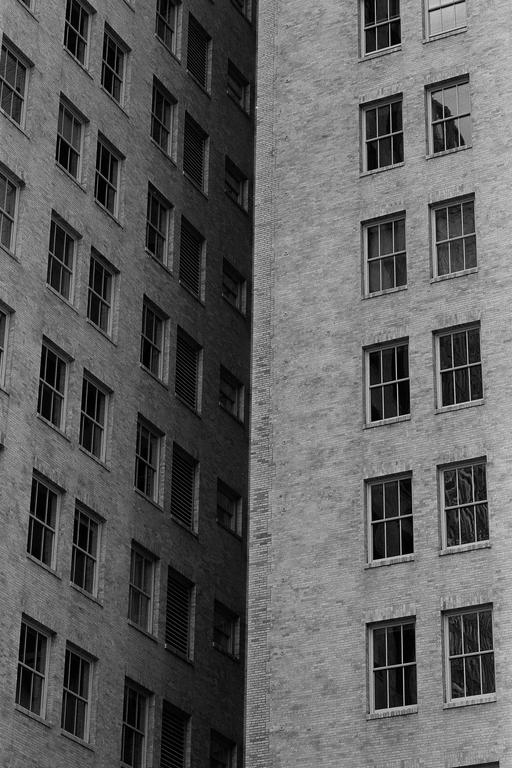 Two brick buildings with many windows are shown from an angle, creating a narrow, dark space between them.