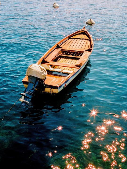 A small wooden boat with an outboard motor floats on sparkling blue water next to two buoys.