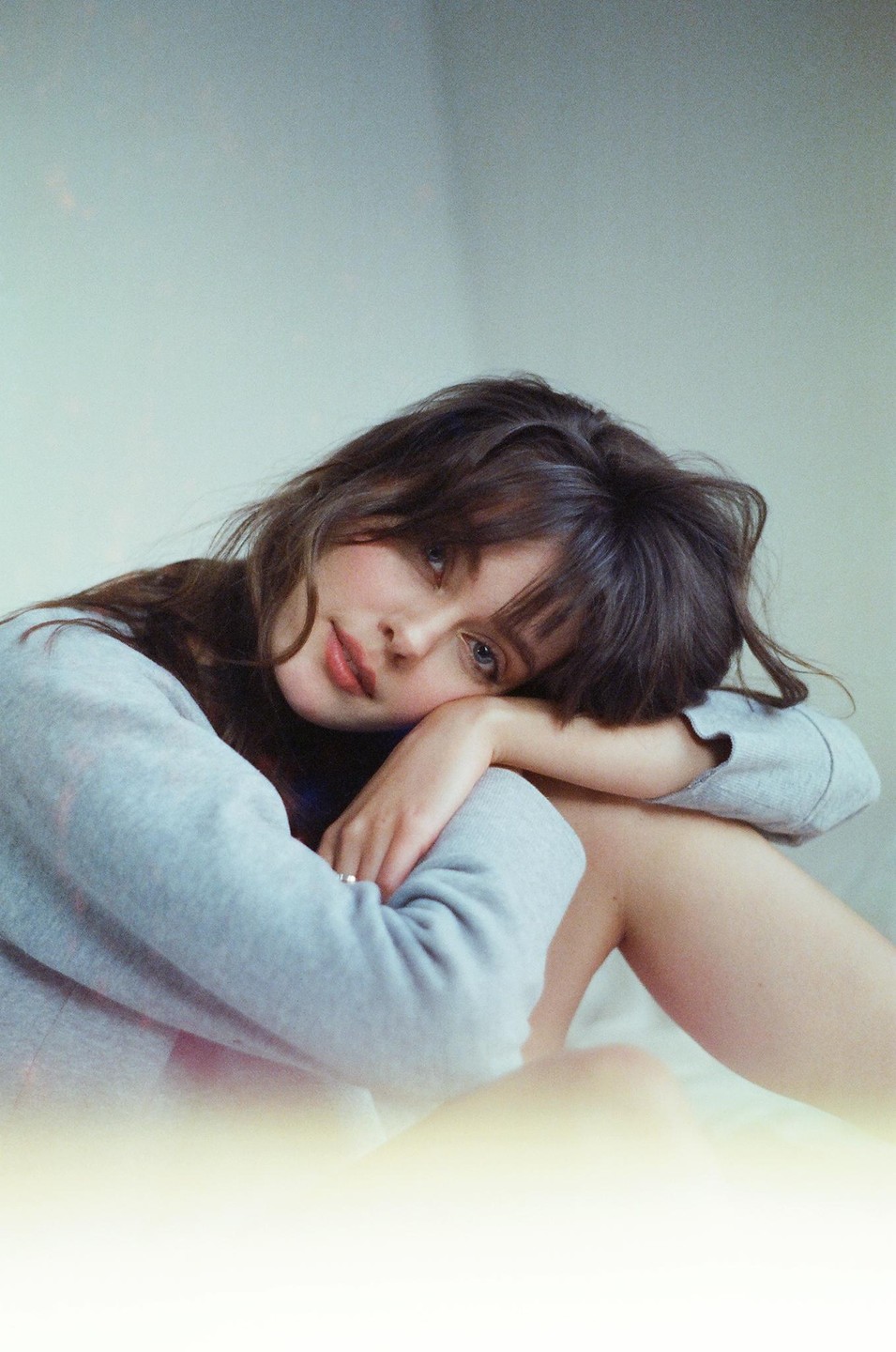 A woman with dark hair and bangs rests her head on her arm while looking at the camera.