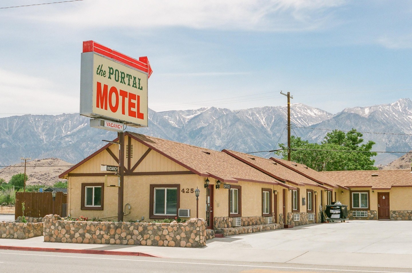 A motel with a large sign stands in front of a mountain range with snow-capped peaks.