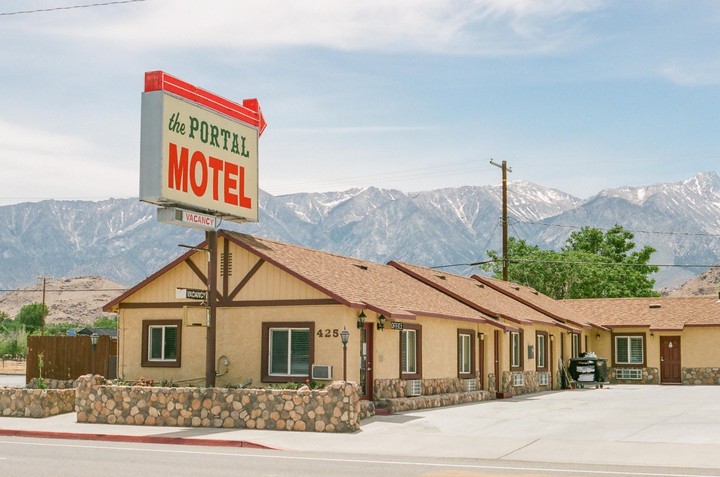 A motel with a large sign stands in front of a mountain range with snow-capped peaks.