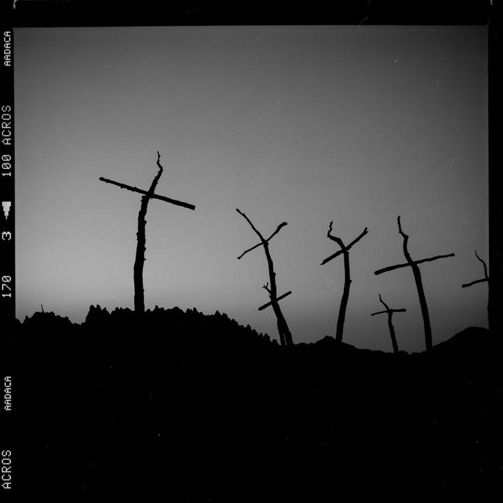 Several silhouetted crosses stand on a hill against a light sky.
