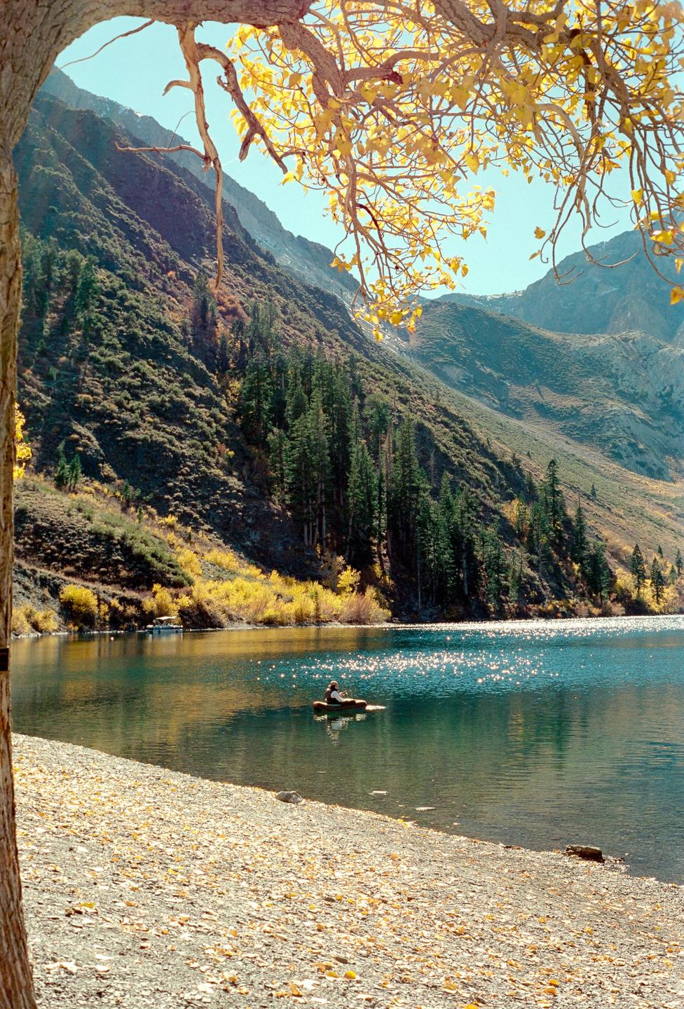 A person in a small boat is on a lake surrounded by mountains with autumn foliage.
