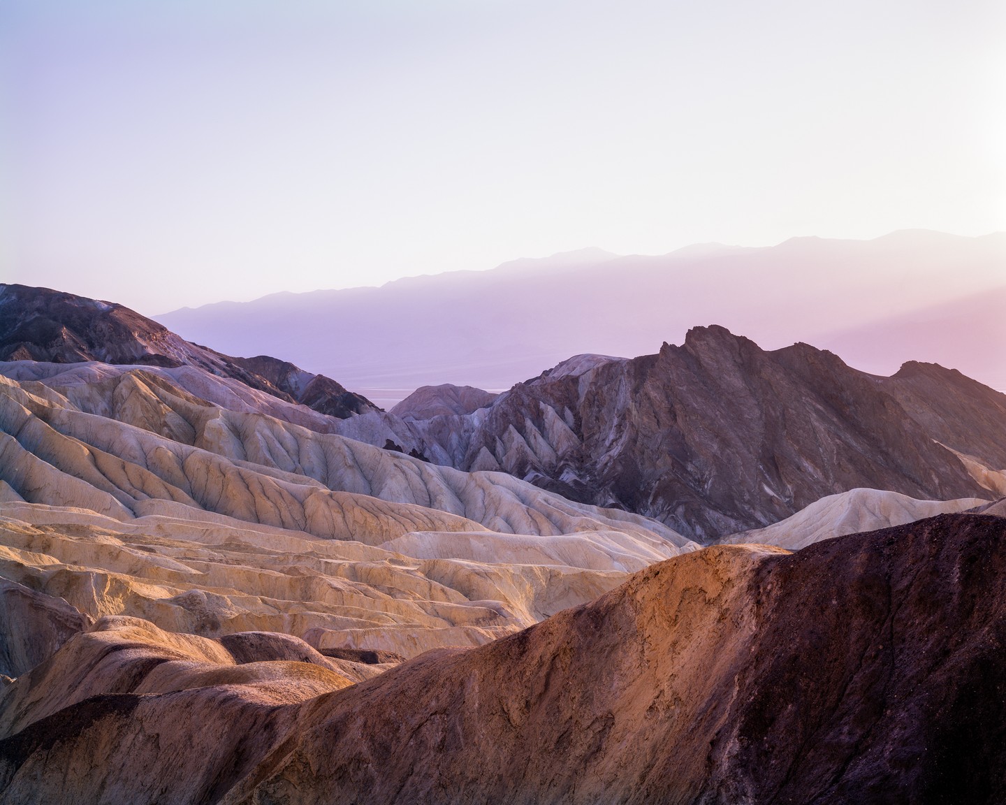 The sun illuminates a desert landscape with mountains and hills under a purple sky.