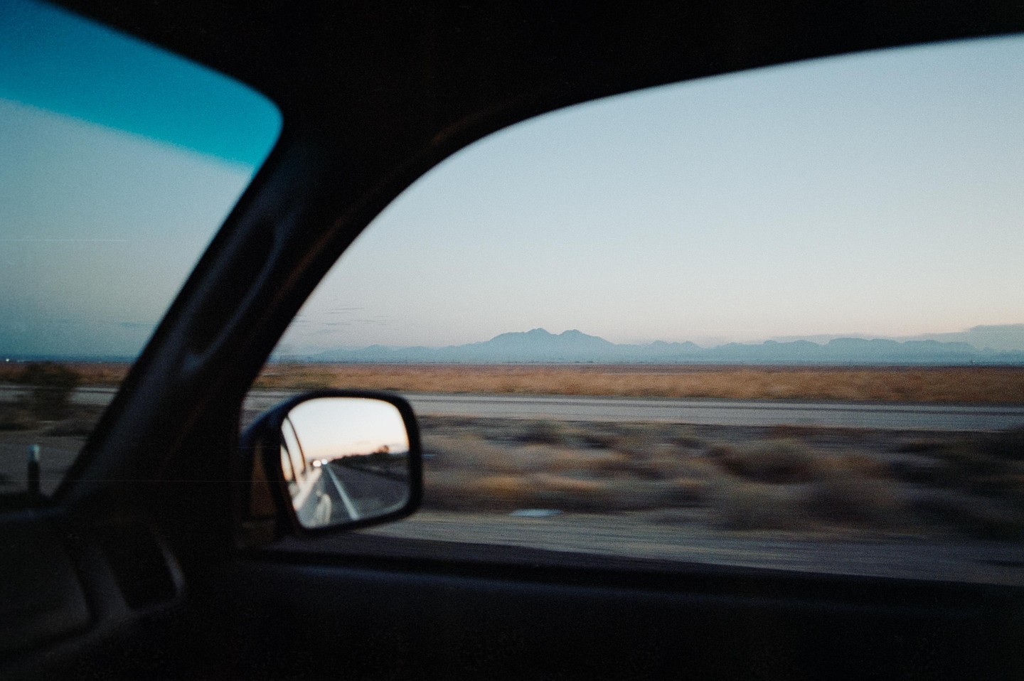 A view from inside a car shows a highway and mountains in the distance at dawn.