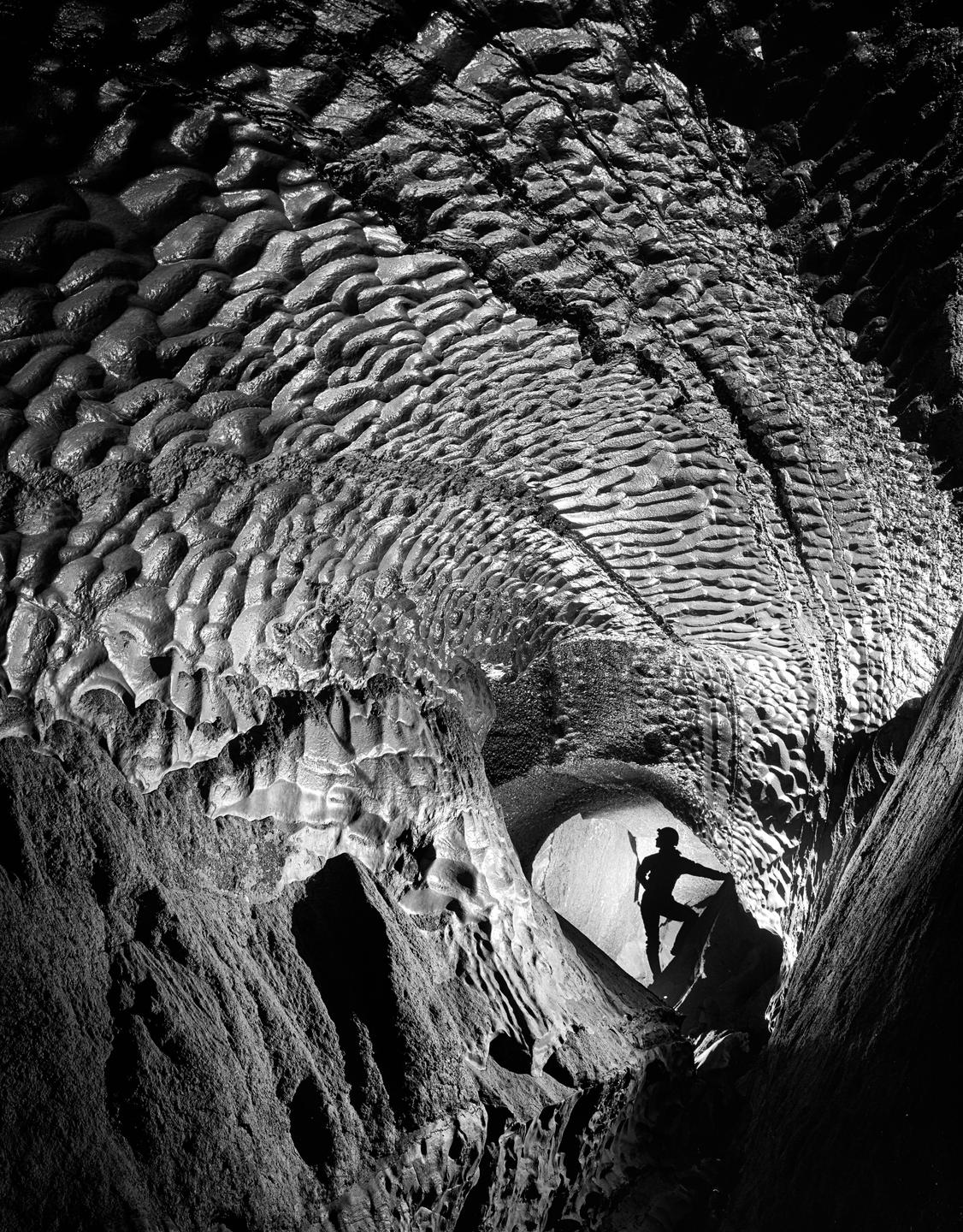 A person stands in a narrow cave passage with textured walls and ceiling.