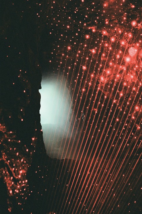 A dark cave opening is illuminated by a bright light and red laser beams.