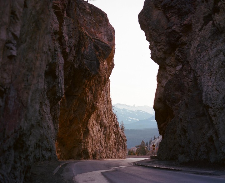 A winding road passes between two large rock formations with snow-capped mountains in the distance.