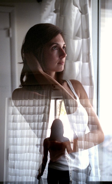 A woman is shown in a double exposure, looking out a window.