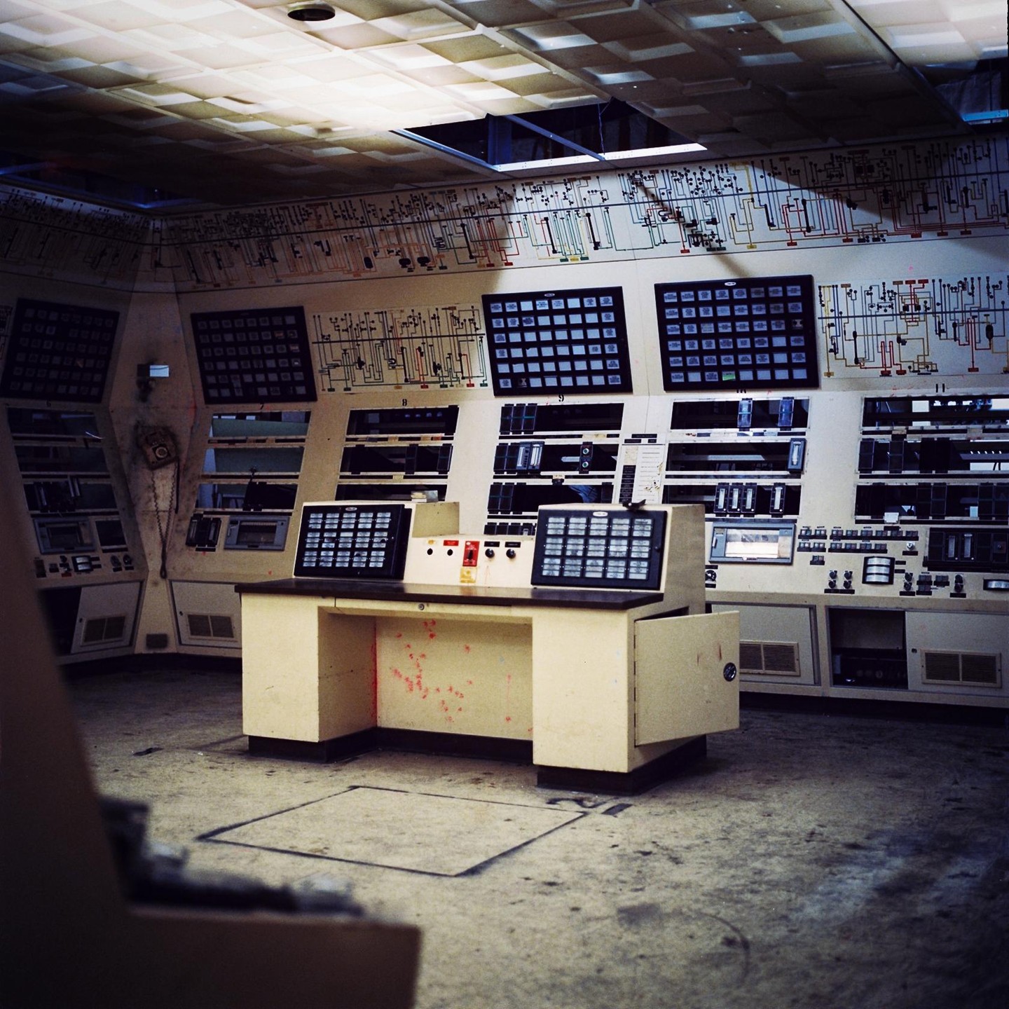 A control room with a large console and many screens is shown from a low angle.