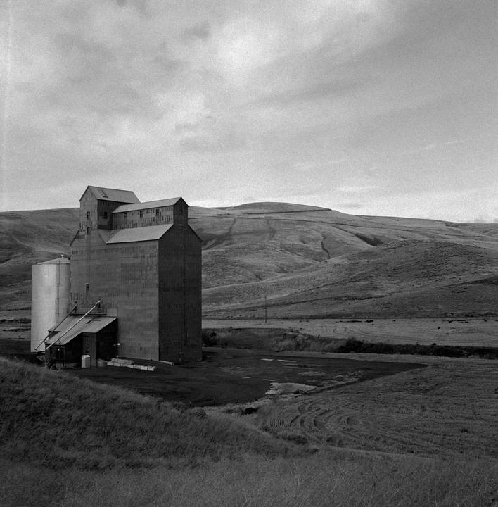 A grain silo stands next to rolling hills under a cloudy sky.