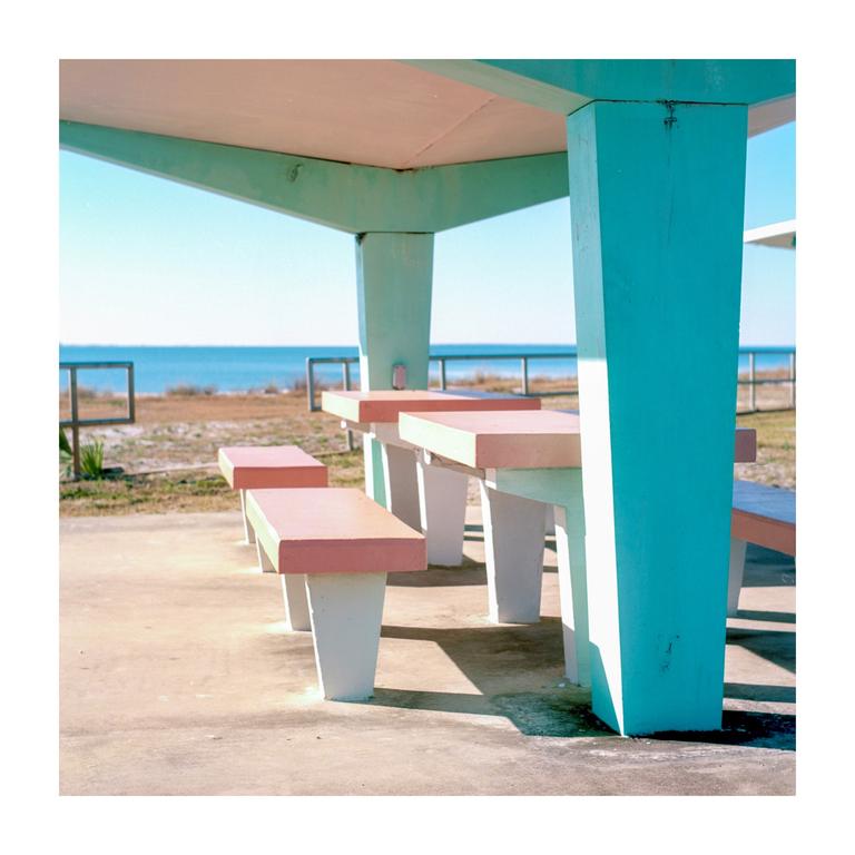 A picnic shelter with pink and teal benches and tables overlooks the ocean.