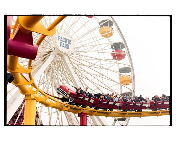 A roller coaster with people on it passes in front of a ferris wheel at an amusement park.