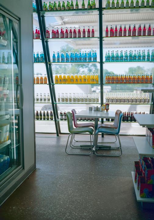 A diner interior features a table with four chairs and shelves filled with colorful bottled drinks.