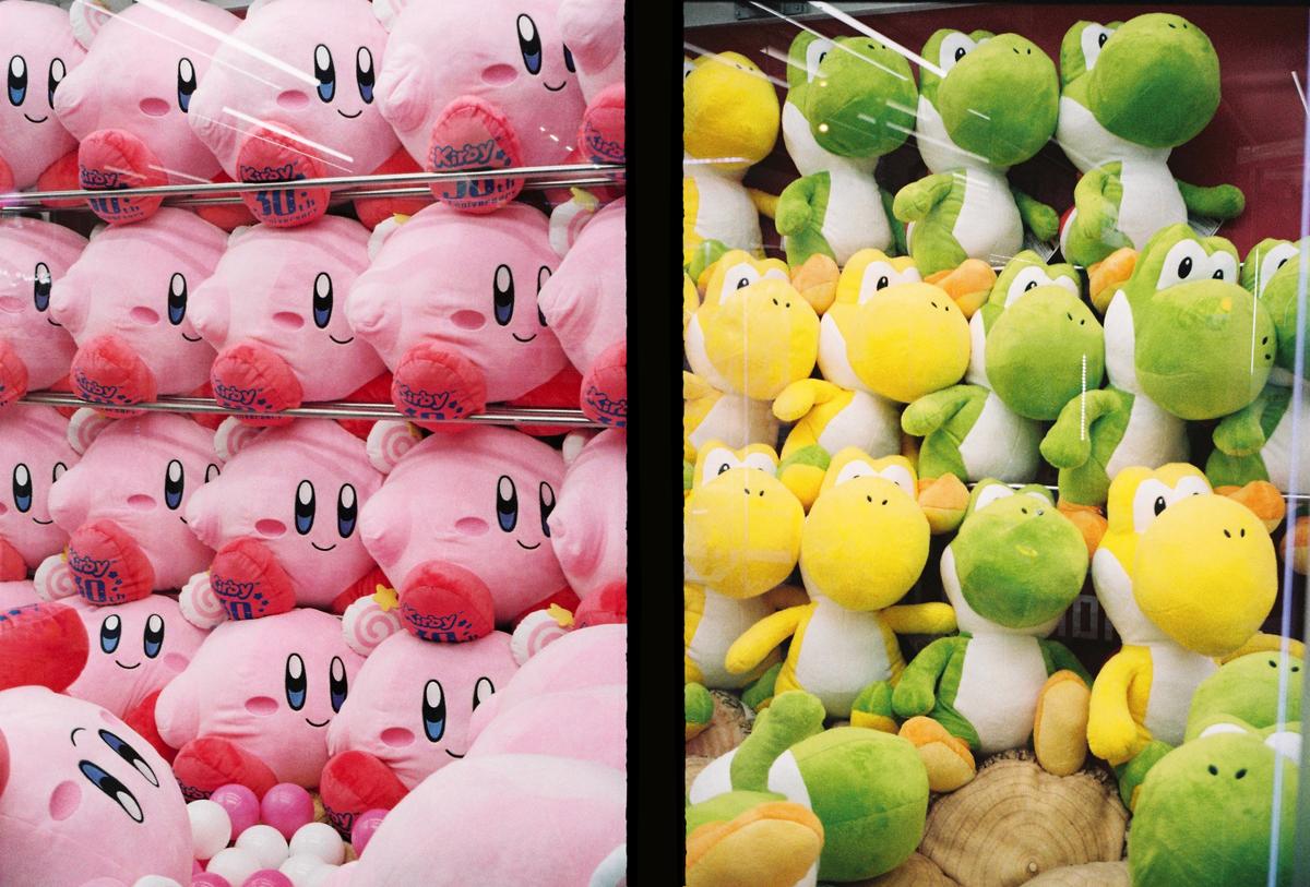 A claw machine is filled with pink Kirby plush toys on the left and green and yellow Yoshi plush toys on the right.