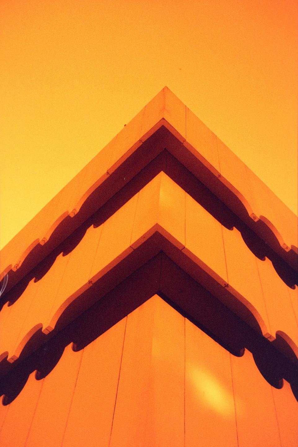 A building with multiple levels and decorative edges is shown from a low angle against a bright sky.