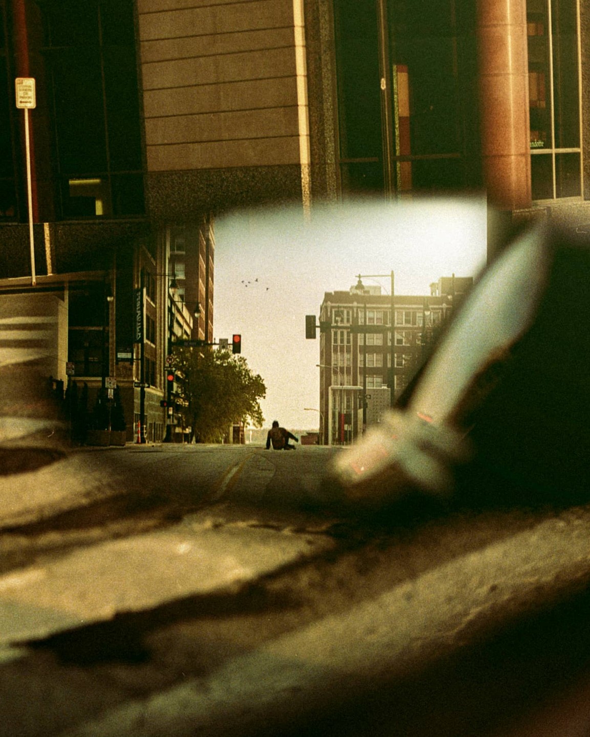 A person sits in the middle of an empty street with tall buildings and a traffic light in the background.