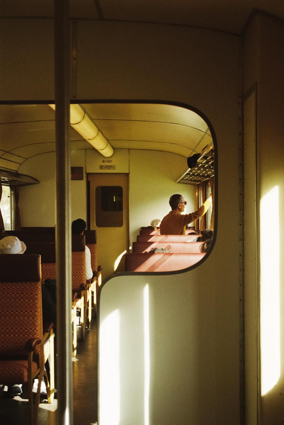 A man looks out a window from inside a train car with sunlight streaming through the windows.