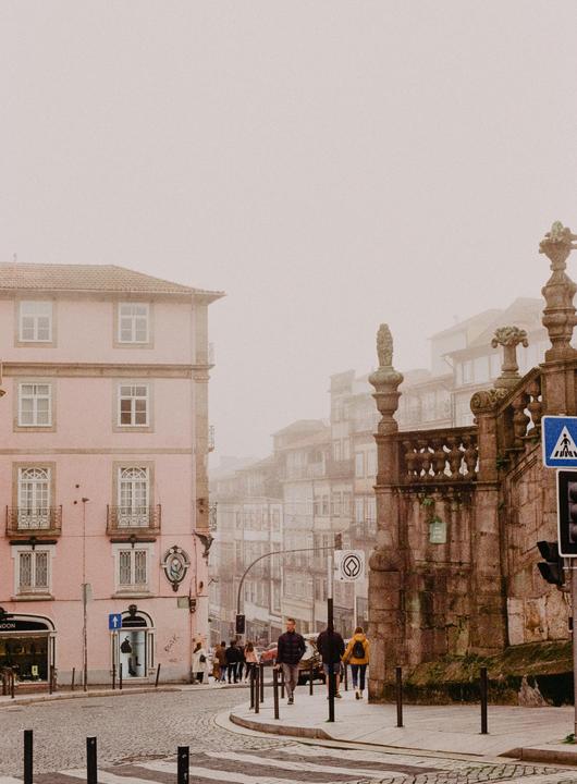 A street in Porto, Portugal is hazy with a pink building on the left and a stone wall on the right.