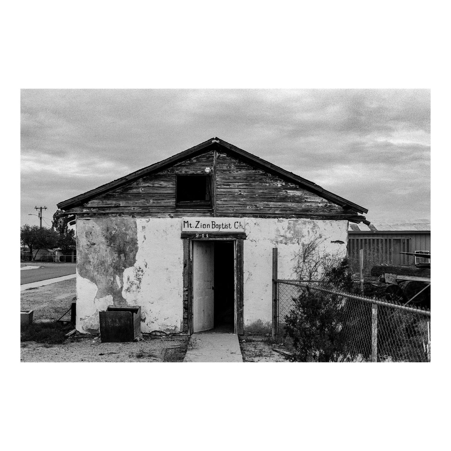 An old, dilapidated building with a sign that reads "Mt. Zion Baptist Ch." stands under a cloudy sky.