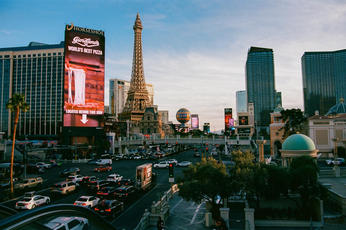 A busy street in Las Vegas is filled with cars and tall buildings, including a replica of the Eiffel Tower.
