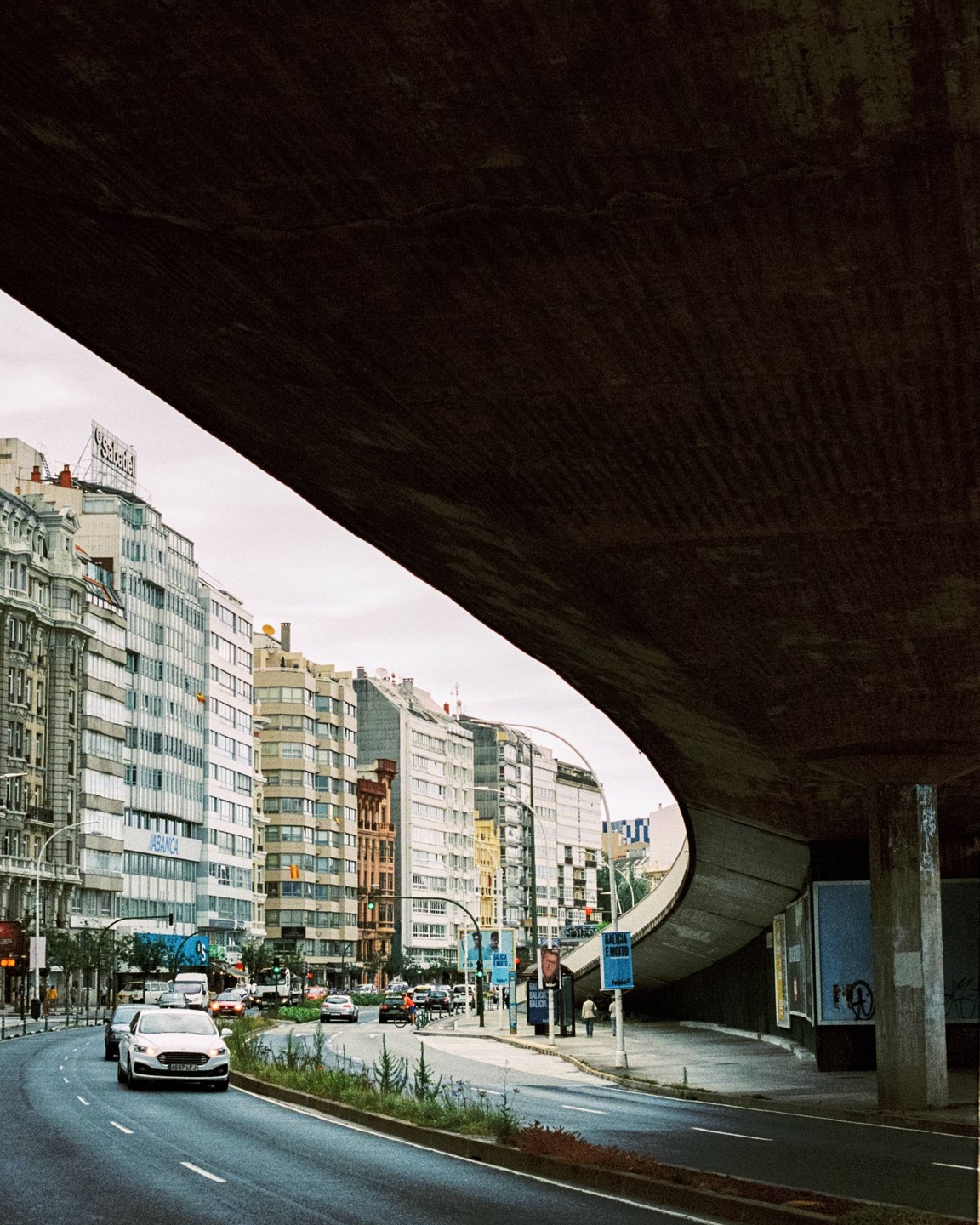 A street with cars and buildings is visible under a concrete overpass.