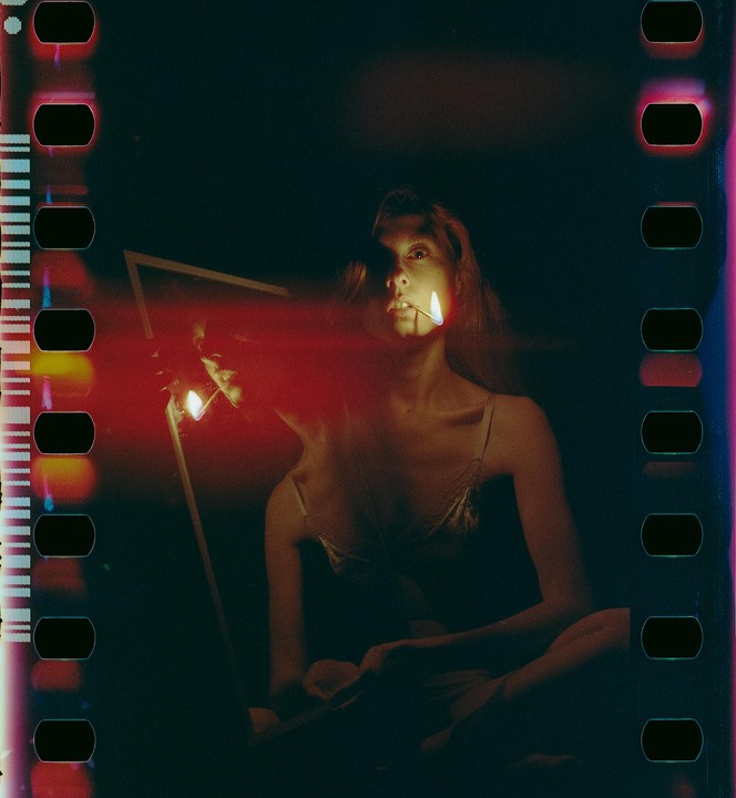 A woman holds a lit match in her mouth while looking into a mirror.