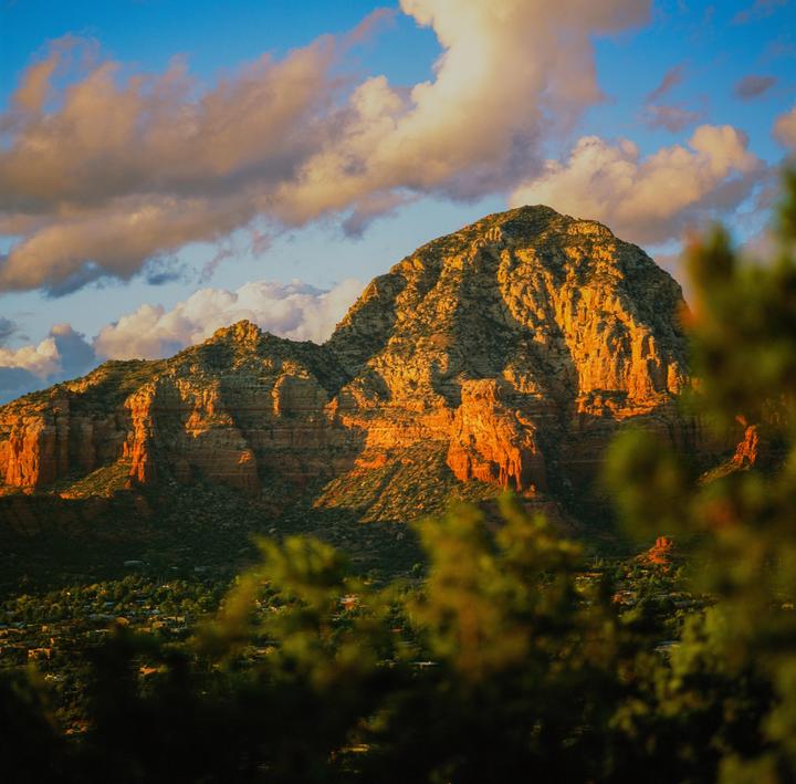 A mountain range is illuminated by golden light under a blue sky with clouds.