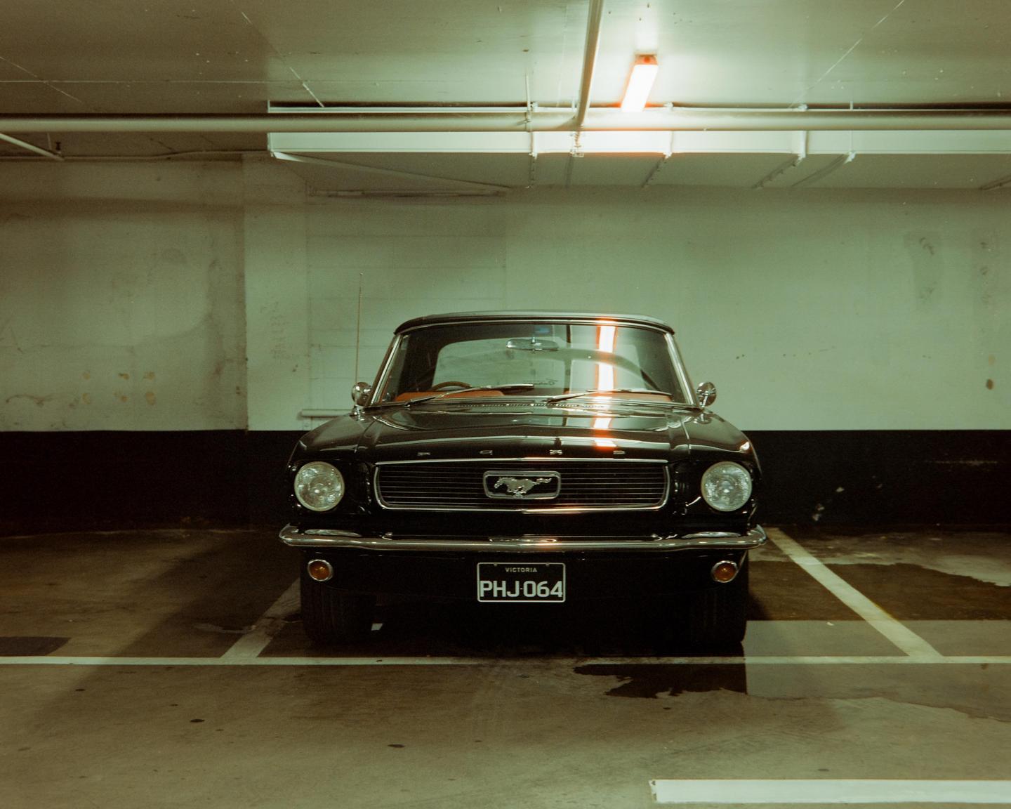 A black mustang is parked in an underground parking garage.