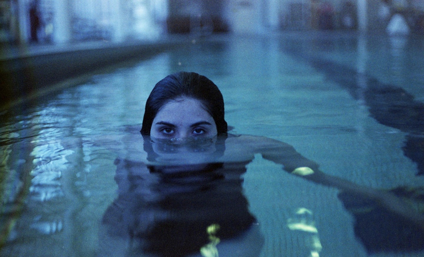 A woman's head is visible above the surface of blue water in a pool.