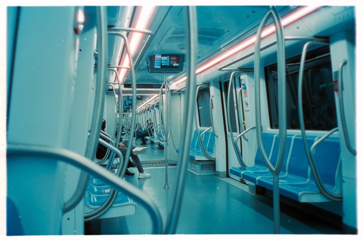 The interior of a subway car is visible, with blue seats and a few passengers sitting down.