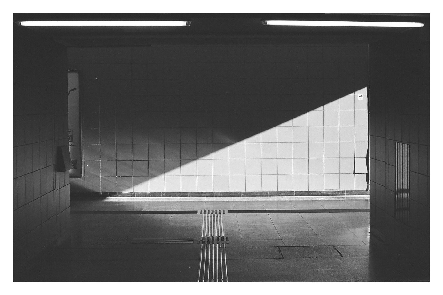 Sunlight casts a diagonal shadow across a tiled wall in a metro station.