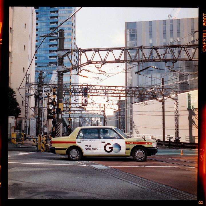A yellow taxi is parked on a city street with tall buildings and power lines in the background.