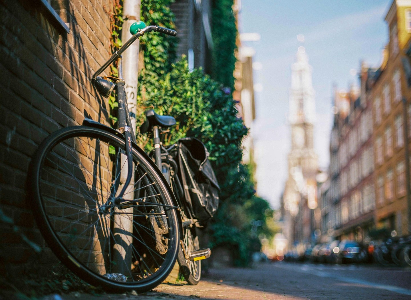 A bicycle is parked against a brick wall with a blurred street and tower in the background.