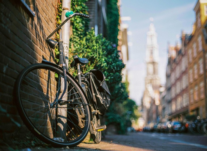 A bicycle is parked against a brick wall with a blurred street and tower in the background.