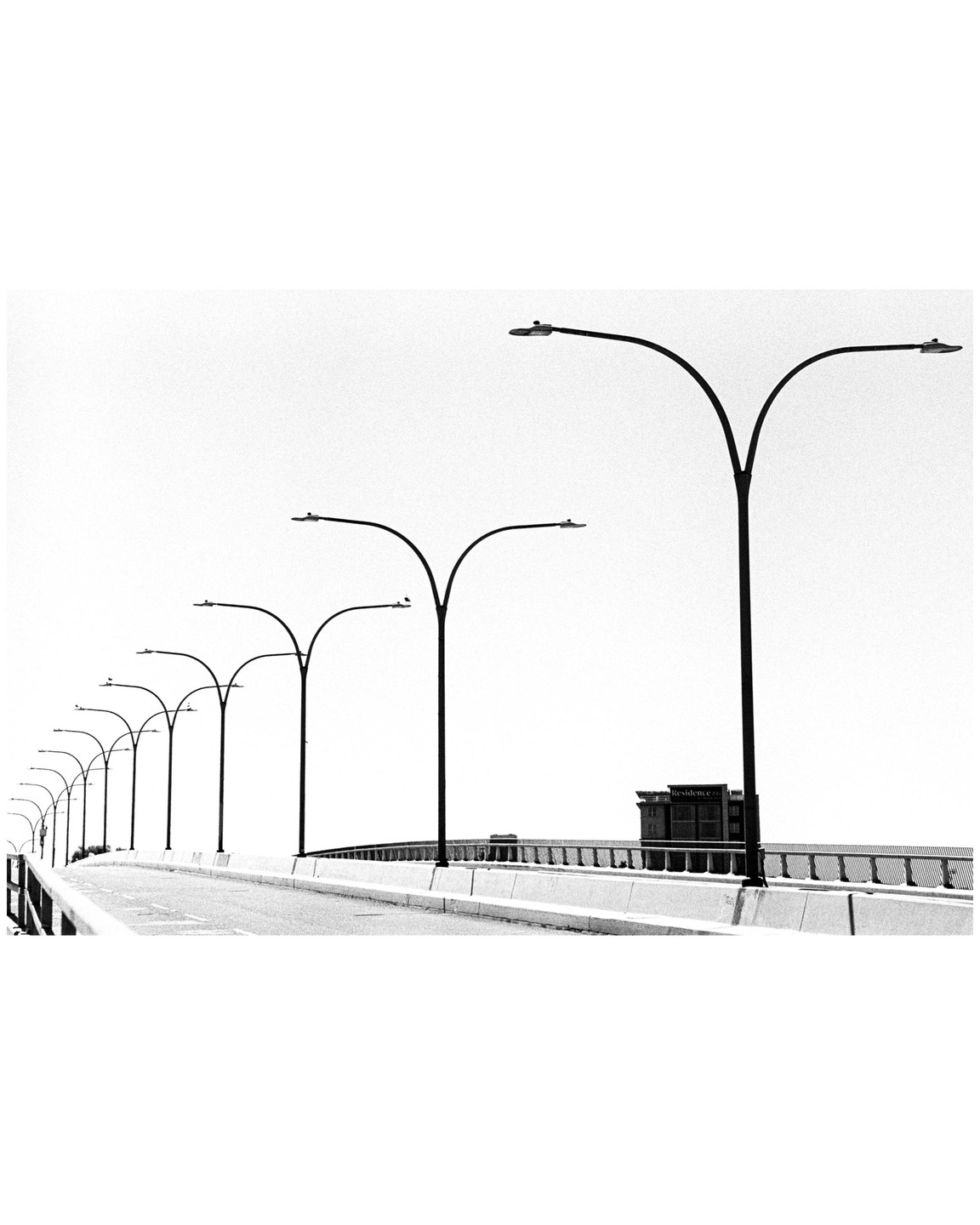 A row of streetlights lines a bridge with a building visible in the distance.