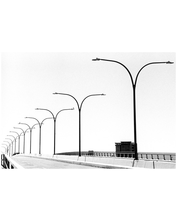 A row of streetlights lines a bridge with a building visible in the distance.