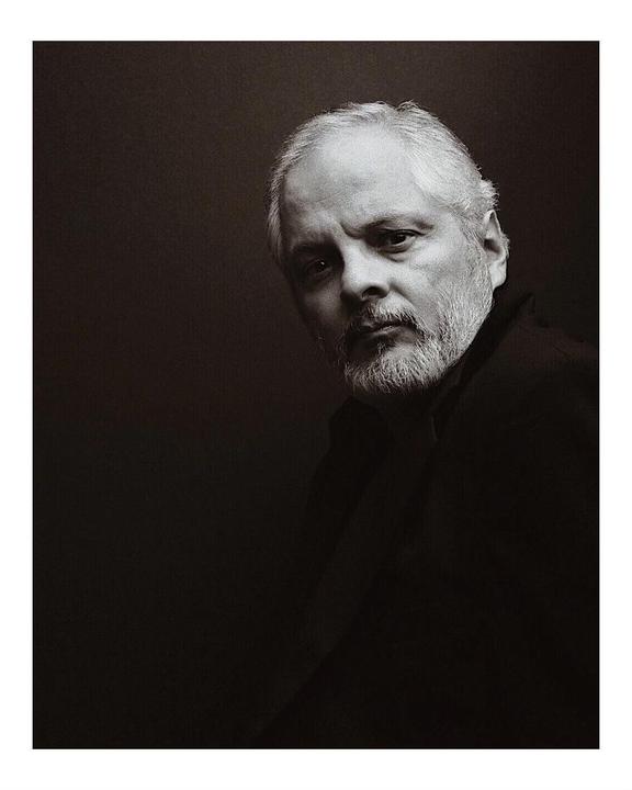 A man with a beard and gray hair looks directly at the viewer in a self-portrait.