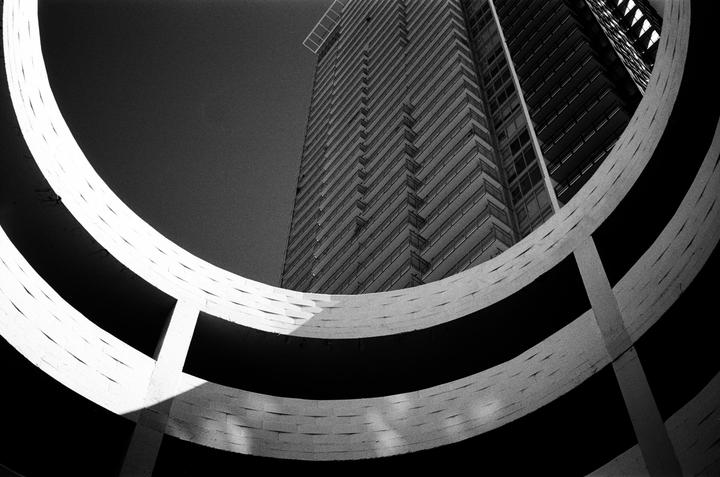 A low-angle view shows a tall building framed by the curved concrete ramps of a parking garage.