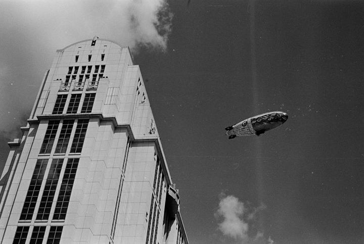 A blimp flies in the sky next to a tall building.
