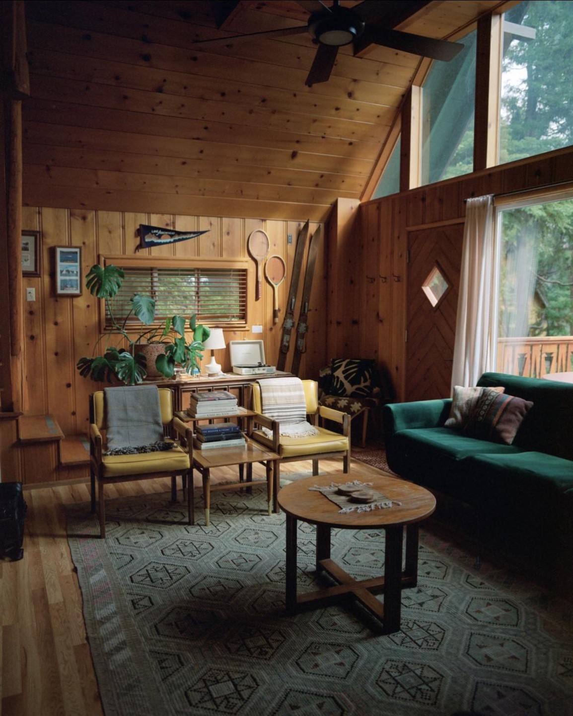 A cozy A-frame cabin living room features wood paneling, a green sofa, and a patterned rug.