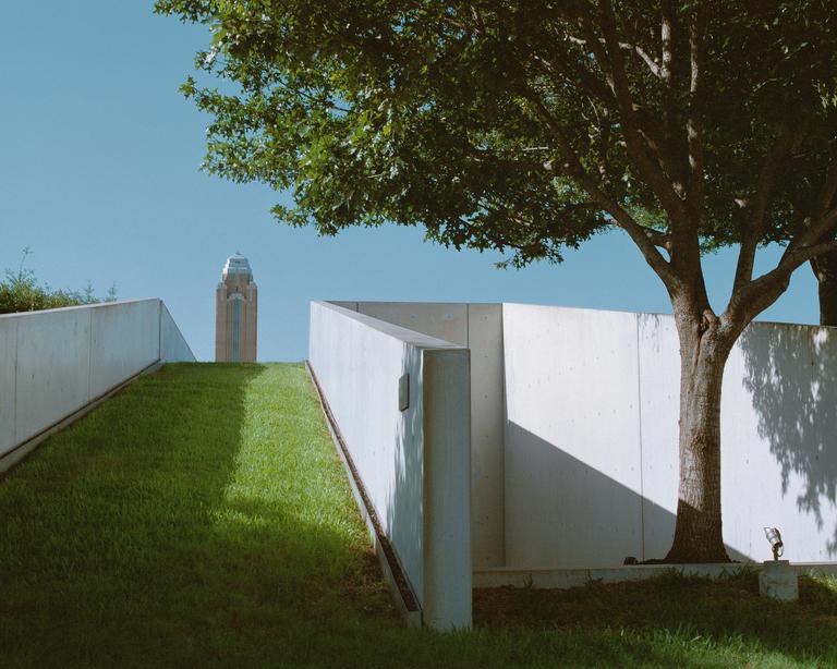 A tall building with a domed roof is visible in the distance beyond a grassy slope and concrete walls.