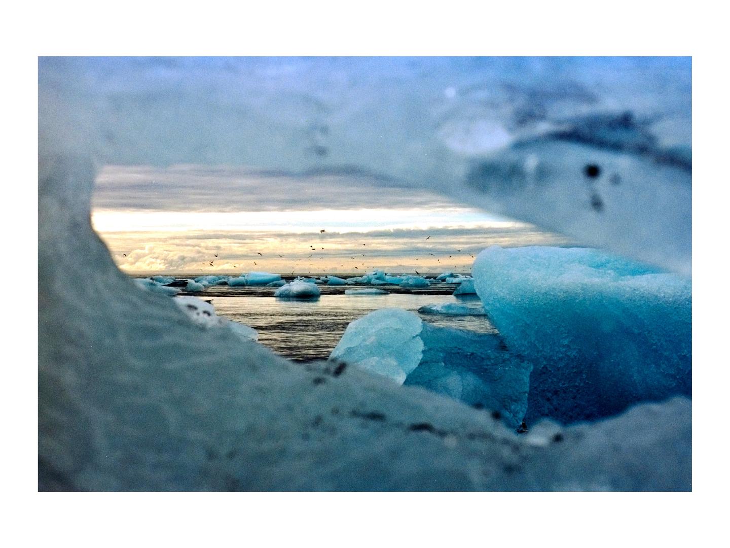 A body of water with icebergs is viewed through a hole in a large piece of ice.