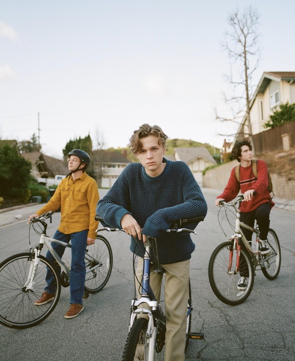 Three boys stand with their bicycles on a residential street.