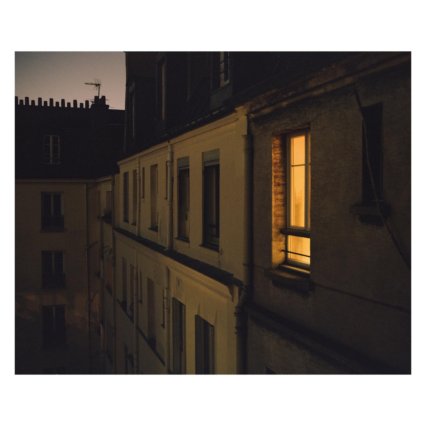 A single illuminated window glows in a dark building at night in Paris.