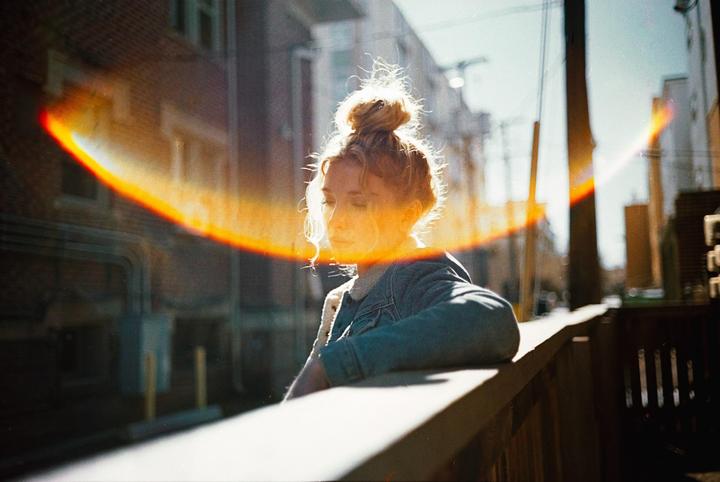 A woman with her hair in a bun leans on a railing with a bright lens flare across the image.